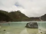 Batu besar di air Kawah Putih, Kabupaten Bandung, dengan lereng kawah di belakangnya.