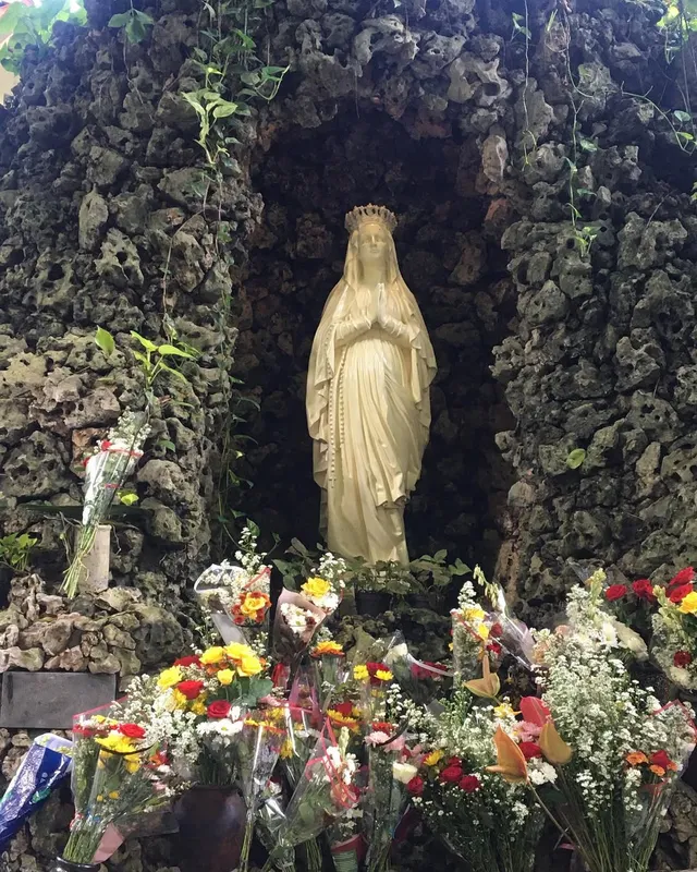 Patung Maria di relung batu Gua Maria Sendangsono dengan bunga di depannya / A statue of Mary in the stone grotto at Sendangsono with flowers in front
