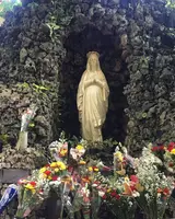 Patung Maria di relung batu Gua Maria Sendangsono dengan bunga di depannya / A statue of Mary in the stone grotto at Sendangsono with flowers in front