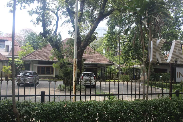 Kapulaga Indonesian Bistro terlihat dari pagar, dengan pepohonan di halaman, Oktober 2024. / Kapulaga Indonesian Bistro seen from the fence, with trees in the courtyard, October 2024.