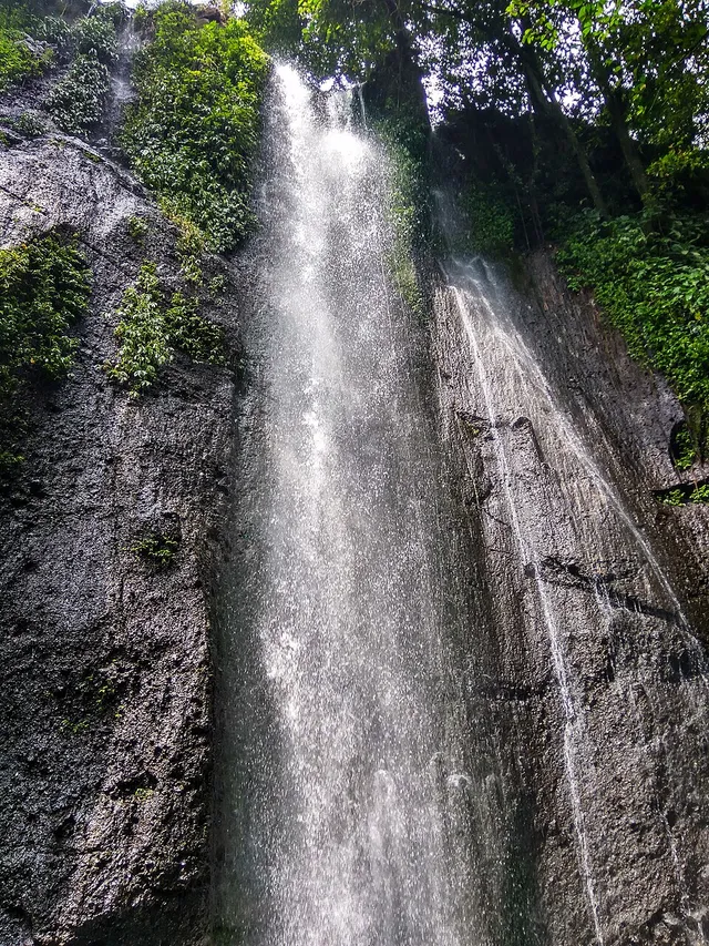Aliran Curug Nangka di antara tebing berbatu dan vegetasi hijau