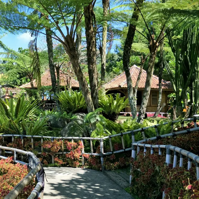 ID: Jalur berpagar bambu di antara taman dan bangunan Floating Market Lembang. EN: A bamboo-railed path among gardens and buildings at Floating Market Lembang.