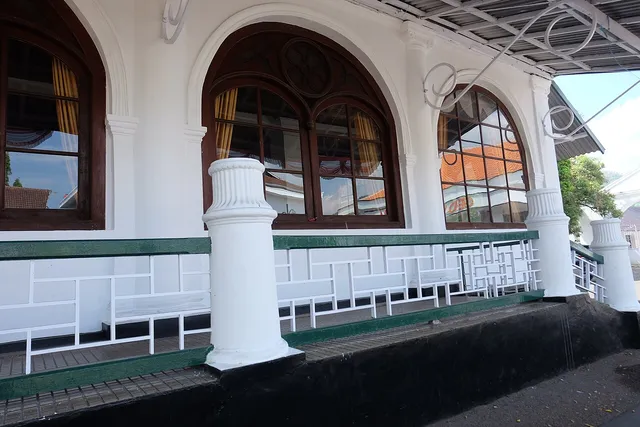 ID: Serambi Gedung Srimanganti dengan pilar putih dan jendela kayu melengkung di Museum Prabu Geusan Ulun. EN: Srimanganti veranda with white pillars and arched wooden windows at Museum Prabu Geusan Ulun.