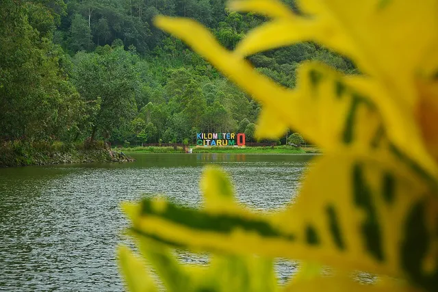 Tulisan Kilometer 0 Citarum di seberang Situ Cisanti dengan daun di latar depan, Maret 2022. / Kilometer 0 Citarum lettering across Lake Cisanti, with foreground leaves, March 2022.