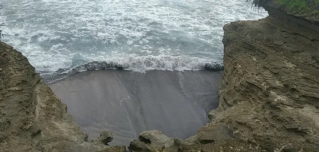 Gelombang masuk ke cekungan pasir dan tebing Pantai Batu Hiu