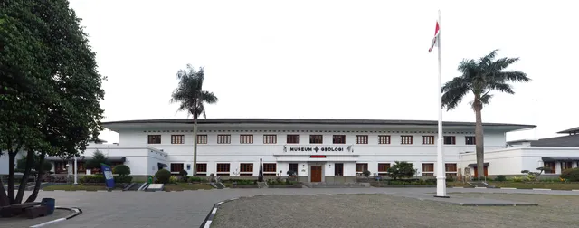 ID: Fasad putih Museum Geologi Bandung dan halaman di depannya. EN: The white facade of Museum Geologi Bandung and its forecourt.